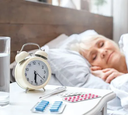 Patientin schläft neben Wecker und Tabletten
