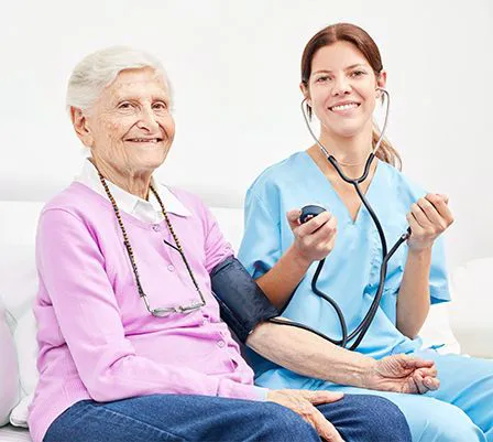 Pflegekraft mit Stetoskop sitzend neben Patientin